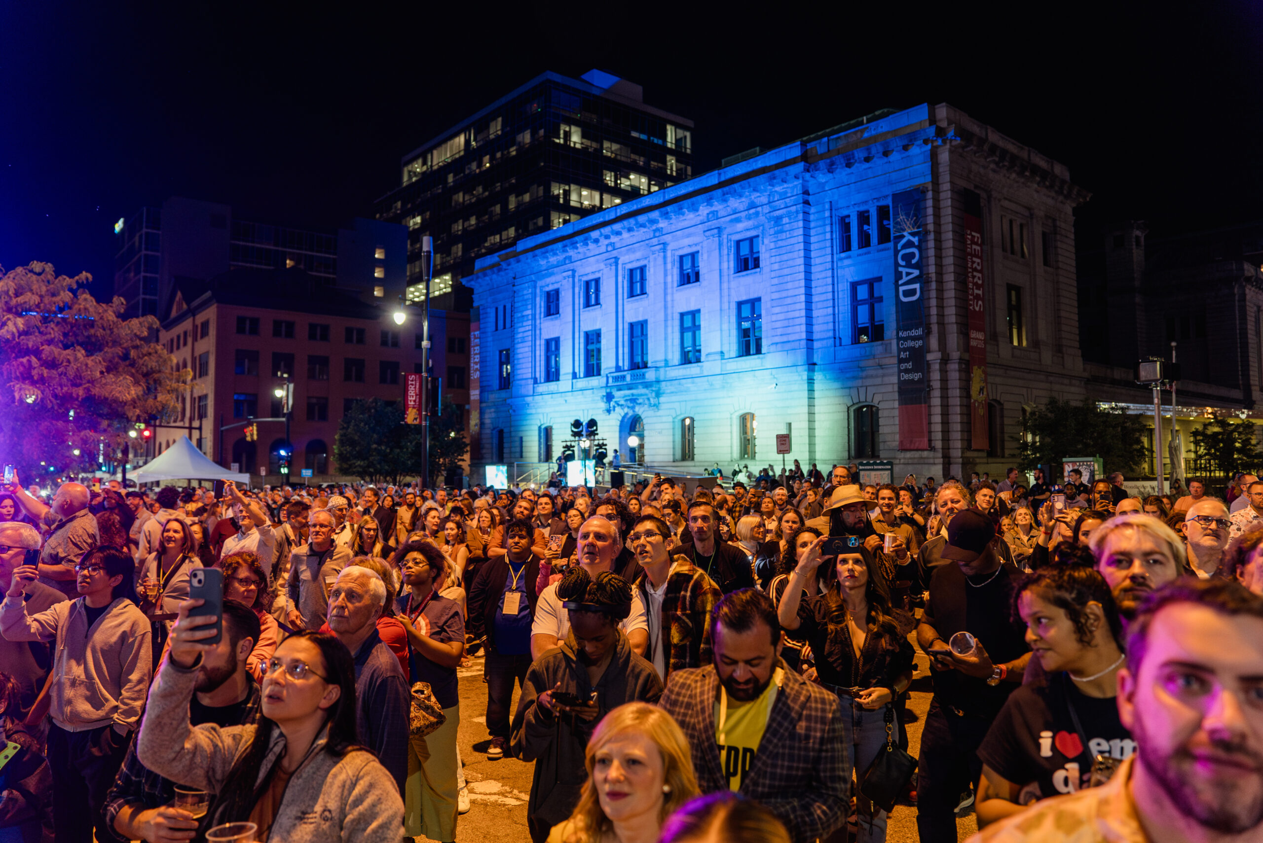 A crowd of people at night in front of a lit-up building.