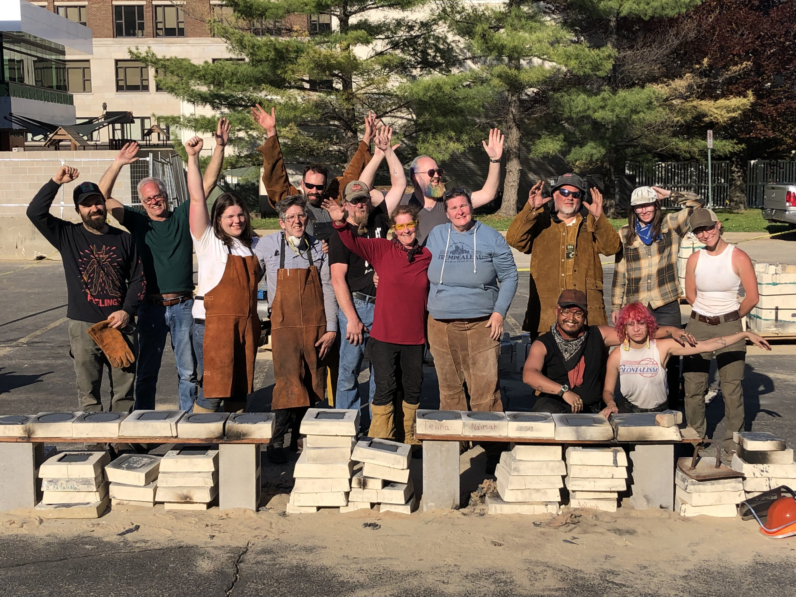 A group of people standing together smiling, waving or holding their arms up.