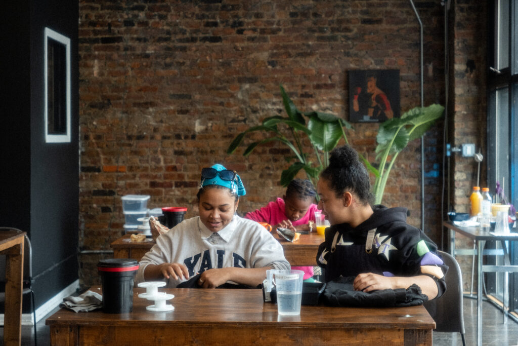 Three people with dark skin sitting at tables with film photography equipment.