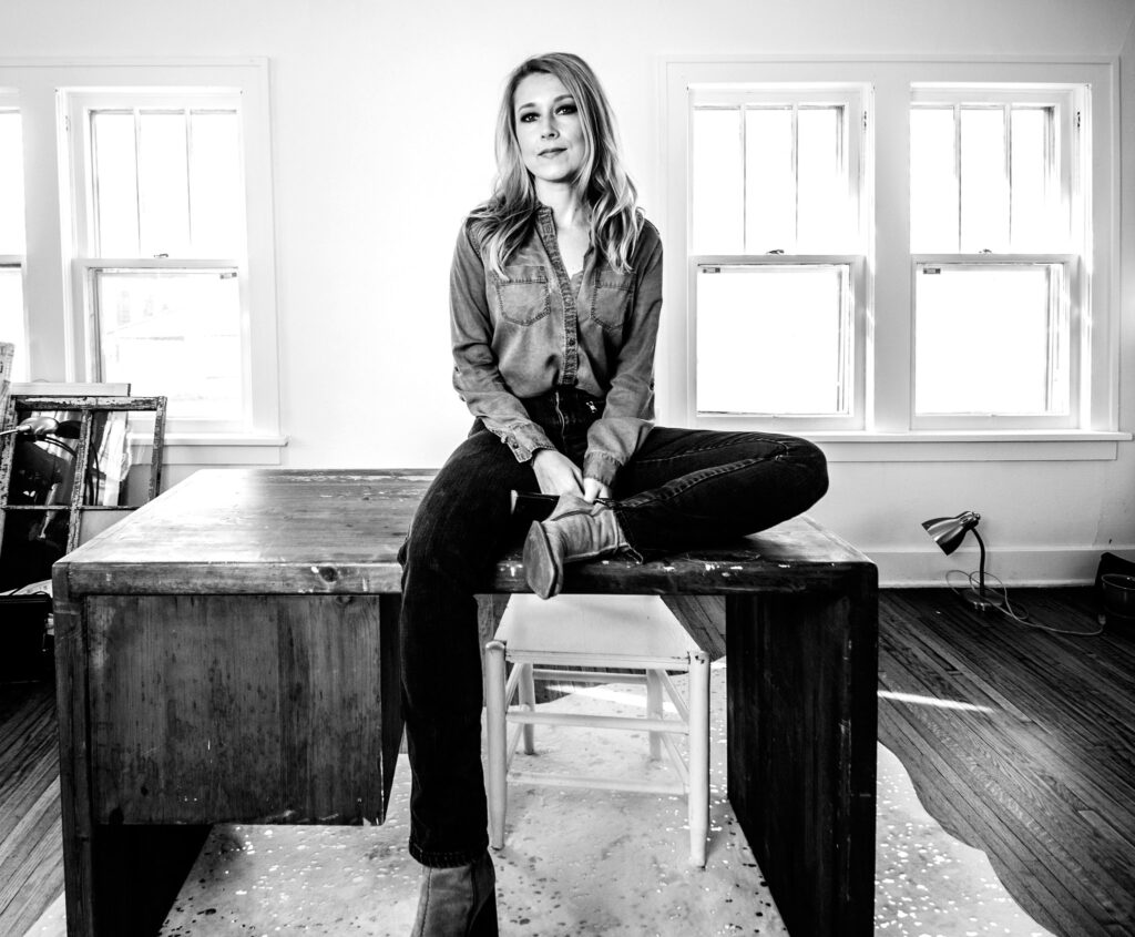A woman sitting on top of a vintage desk in a well-lit room.